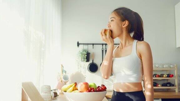 亚洲活跃迷人的女子穿着运动服在厨房吃苹果年轻漂亮的女孩心情愉快喜欢吃水果健康的食品饮食和减肥的保健在家里