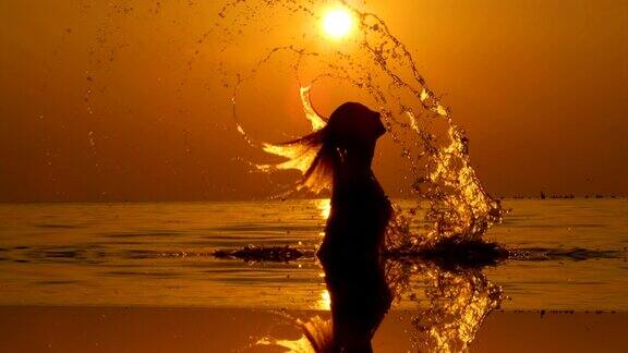 慢镜头:日落时分一名年轻女子用头发溅起海水