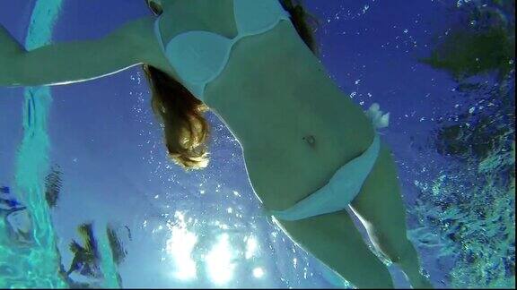 苗条漂亮的女孩穿着白色泳衣在水下游泳在阳光下