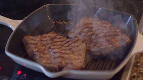 一块牛排在烤盘上煎着煎锅上冒出白烟