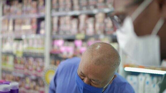 年轻的药剂师在药店帮一位年长的人戴着口罩