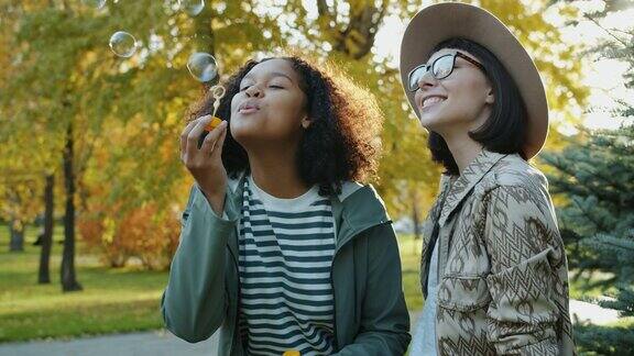 快乐的学生女孩吹肥皂泡在公园里玩的慢镜头