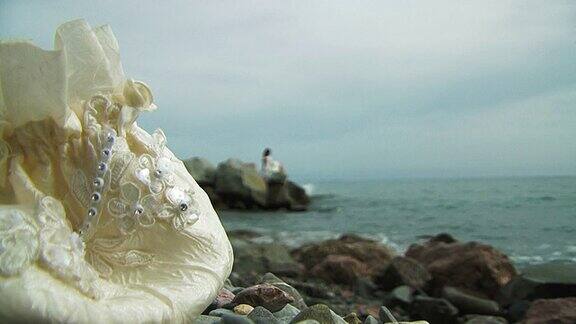 穿着白色连衣裙的年轻女子坐在海边的岩石上