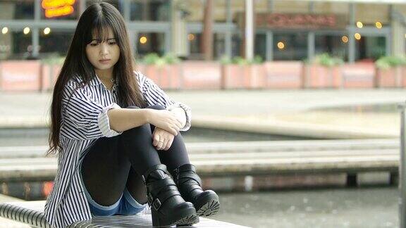 悲伤的中国年轻成年女子独自坐在城市的长椅上