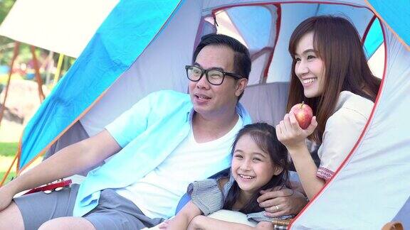 4K快乐的年轻亚洲家庭享受露营在湖一对父母和可爱的小女孩的家庭坐在帐篷前的早上在假期一起玩