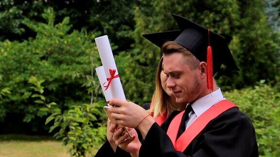 微笑的男女毕业生拿着文凭用手机自拍
