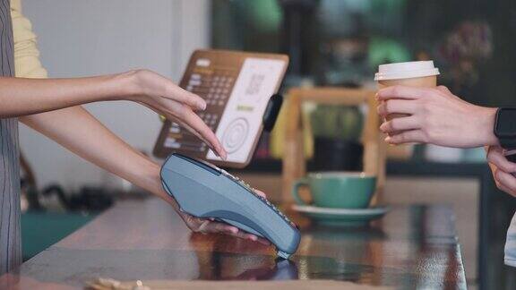 关闭客户使用信用卡支付在信用卡机上非接触和接受咖啡杯从柜台酒吧的咖啡师在咖啡馆无线支付生活