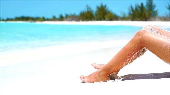 女性苗条的晒黑的腿在一个白色的热带海滩缓慢的视频