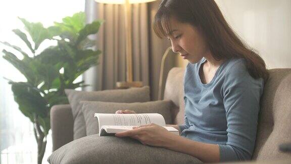 亚洲妇女坐在沙发和读书在家里