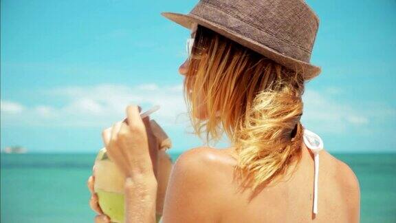 女人喝新鲜的椰子水与吸管在海滩有趣的假期3杯