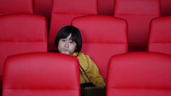 一个亚洲华裔女孩一边吃着薯条一边独自在电影院看电影