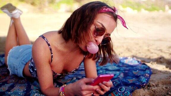 一个年轻女人在沙滩上吹泡泡发短信