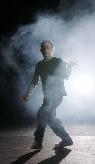 垂直视频的年轻女舞者表演嘻哈舞蹈在慢动作与光和烟的背景