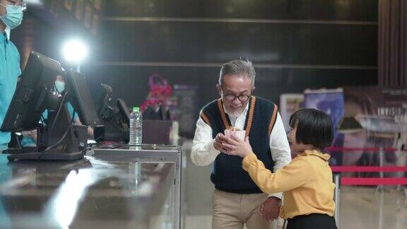 亚洲的中国爷爷孙女在电影院放映前用非接触式付款购买爆米花