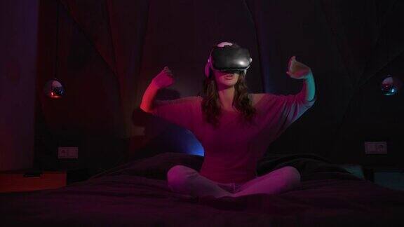 年轻女子坐在黑暗房间的床上戴着虚拟或增强现实眼镜
