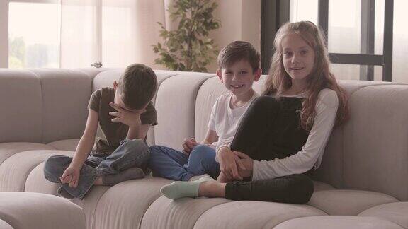 可爱的姐姐和两个可爱的弟弟坐在沙发上看着镜头的肖像