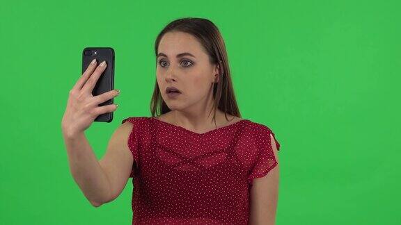 一个身穿红裙的柔弱女孩的肖像正在用手机进行视频聊天不满意绿屏