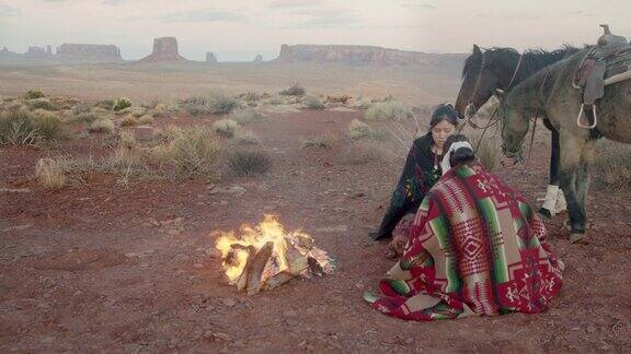 两个美国土著姐妹一个在打鼓裹着传统的纳瓦霍毯子在篝火旁取暖标志性的纪念碑日落
