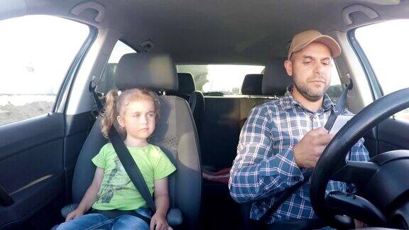 父亲和他的小女儿正在开车不称职的父母在开车时使用智能手机一个男人边开车边发短信车上还有他女儿
