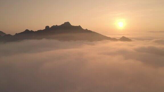 无人机在雾和云层中飞行的视频在山顶在雾之上看到太阳在前面