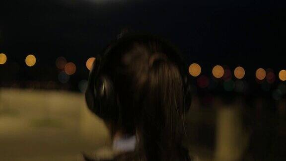 女孩戴上耳机开始在夜晚在城市中奔跑运动员在月光下训练