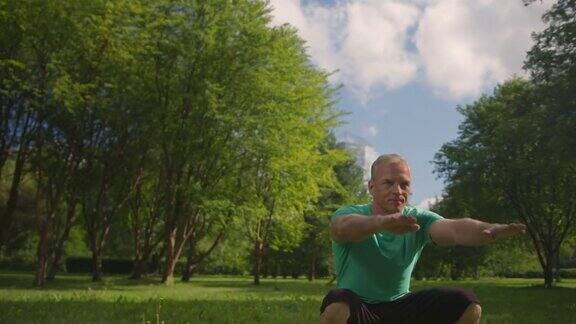 在清晨的阳光下一个穿着蓝绿色t恤的中年斯堪的纳维亚运动员蹲在一个公园里