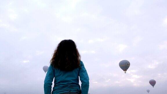小女孩正在土耳其卡帕多西亚的戈雷米观看热气球飞行