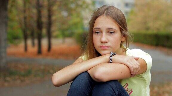 悲伤而忧郁的少女坐在秋天的公园里