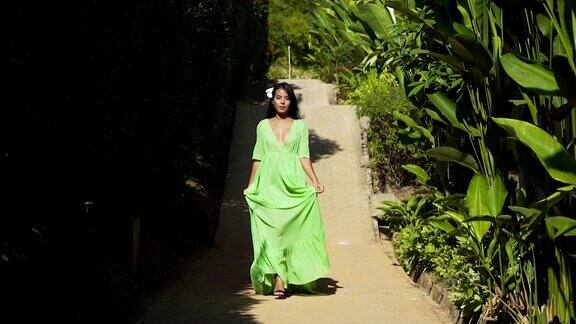 一个亚洲模特在绿色的裙子去在热带加登的道路