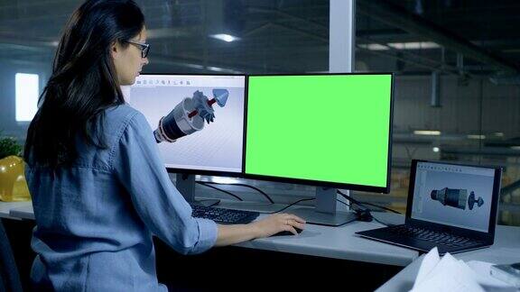 专业女性工程师设计3D涡轮发动机为一个大的工业公司她的第二个显示器显示模拟绿色屏幕计算机从办公室的窗户望出去可以看到一个大工厂