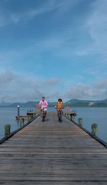一对男女在泰国KohYaoYai海边的一个木制码头上骑自行车男男女女在海滩上骑自行车