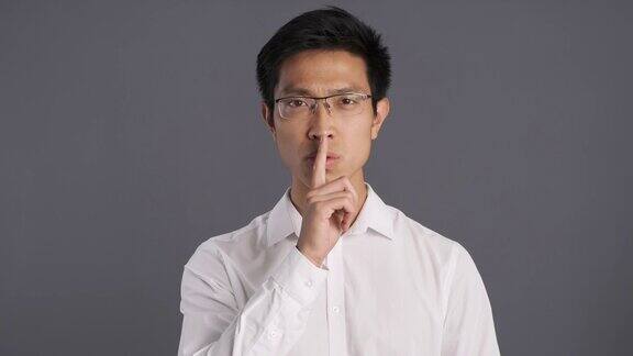 年轻严肃的亚洲男子戴着眼镜在灰色背景下显示沉默的姿态