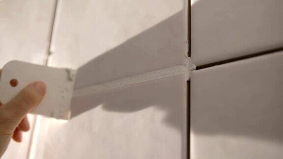 在浴室墙上贴瓷砖的工人他的手把瓷砖放在粘合剂上