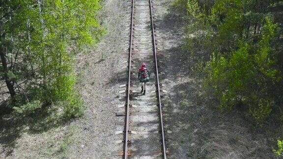 一个背着背包的游客沿着森林地区的铁路走无人机的视角