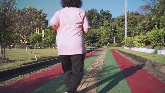 在一个阳光明媚的日子里亚洲老年肥胖女性在公园的跑道上慢动作跑步退休生活方式的活动医疗动机脉搏血压跟踪后视镜