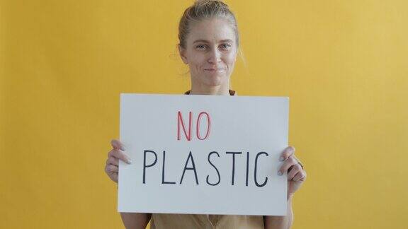 女性活动家的肖像拿着拒绝塑料的标志在黄色的背景上微笑