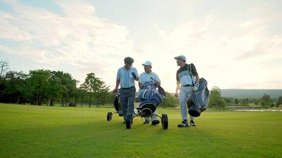 4K集团亚洲商人和高级CEO拿着高尔夫球袋在夏日夕阳下一起走在高尔夫球道上