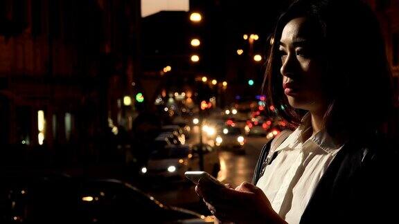 一名悲伤的年轻中国女子的个人资料专注于晚上在智能手机上打字