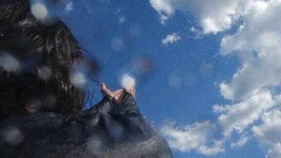 难以辨认的流浪者在沙漠中享受期待已久的雨一个黑头发的瘦弱男子向天空伸出双臂雨点落在他身上200帧秒的慢动作