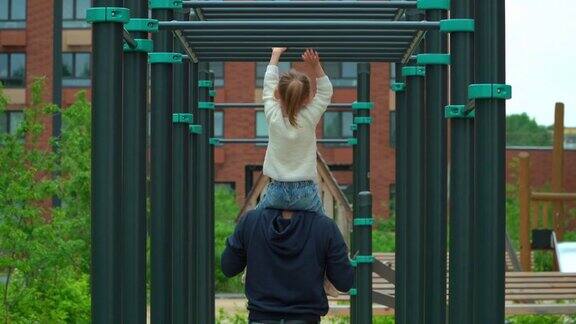 爸爸和小女孩在户外操场上做运动的背影快乐的家庭孩子和爸爸在夏天的公园里玩活跃的游戏
