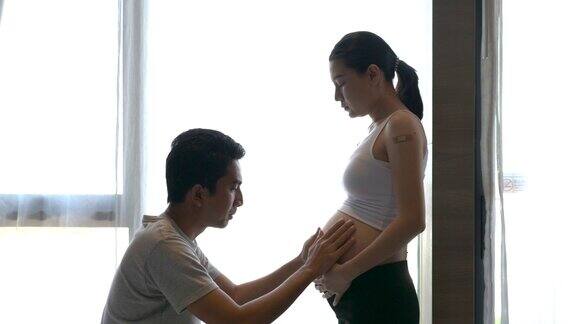 亚洲孕妇夫妇在家里的客厅触摸和倾听肚子