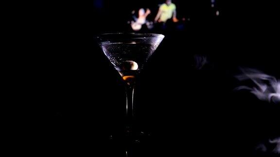 滑块杯中有橄榄的马提尼近距离观看与俱乐部的酒在黑暗的雾色调的背景有选择性的重点酒精饮料倒入马提尼杯的瓶子俱乐部饮料
