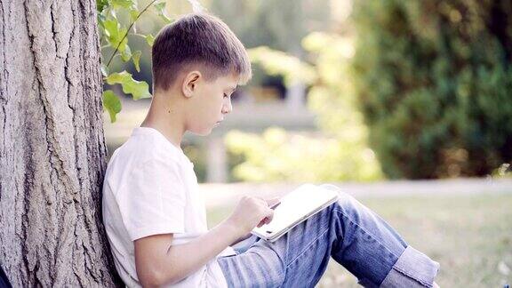 一个十几岁的男孩坐在草地上用着平板电脑