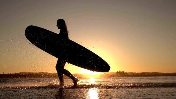 慢镜头:日落时冲浪女孩在浅海中奔跑溅起水花