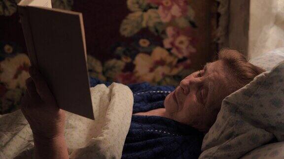 一位上了年纪的妇女正躺在床上盖着毯子看书