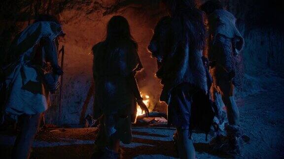 穿着兽皮的史前狩猎采集者部落晚上住在洞穴里尼安德特人或智人家庭试图在篝火前取暖手放在火上在后视图
