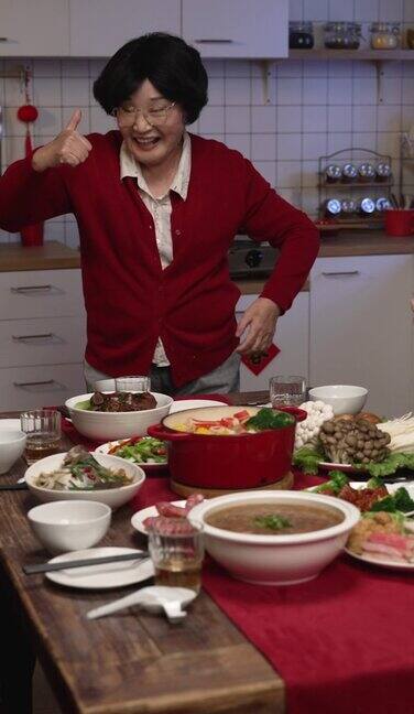 竖屏:穿着红色衣服的老奶奶在端菜时竖起大拇指为自己的厨艺感到骄傲为中国农历新年的团圆饭做准备翻译:春天