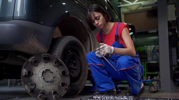 年轻的女机械师正在一家修理店给一辆汽车换轮胎