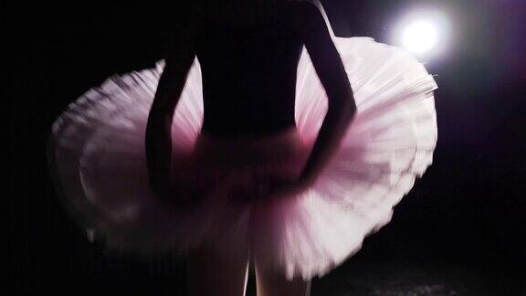 芭蕾舞演员在工作室黑色背景下的聚光灯下表演脚尖旋转慢动作