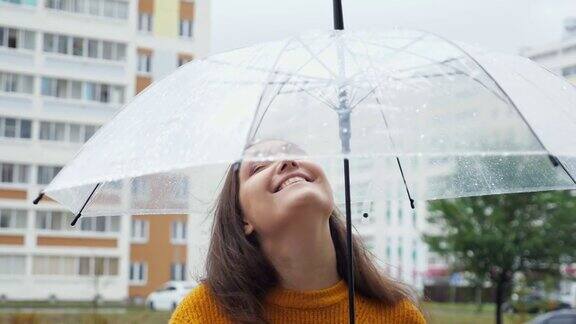 快乐的年轻女子站在雨中透明的伞下